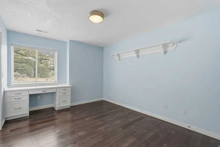 Built-in desk with cabinetry, wood-finish flooring, overhead lighting, and wall-mounted shelving