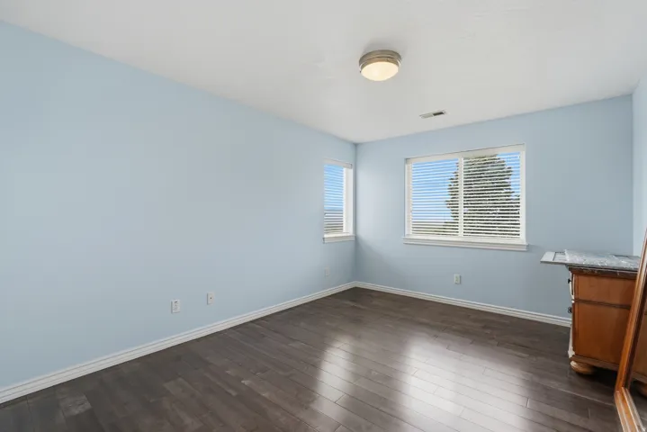 Wood-finish flooring, light blue painted walls, two windows with blinds, and a flush mount ceiling light fixture