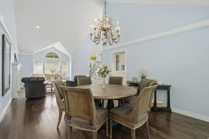 Spacious living area featuring high vaulted ceilings, elegant dark wood-finish flooring, a decorative chandelier, and a prominent arched window