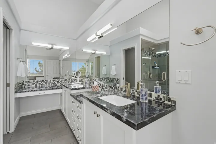 Dual vanity with dark stone countertops, under-mount sinks, and mosaic tile backsplash