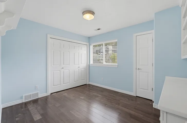 Wood-finish flooring, white trim, and a window with horizontal blinds provide natural light