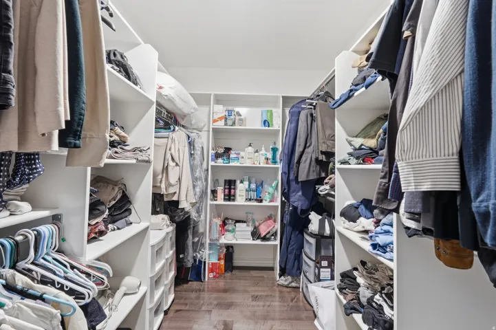 Walk-in closet featuring built-in white shelving, hanging rods, and wood-finish flooring