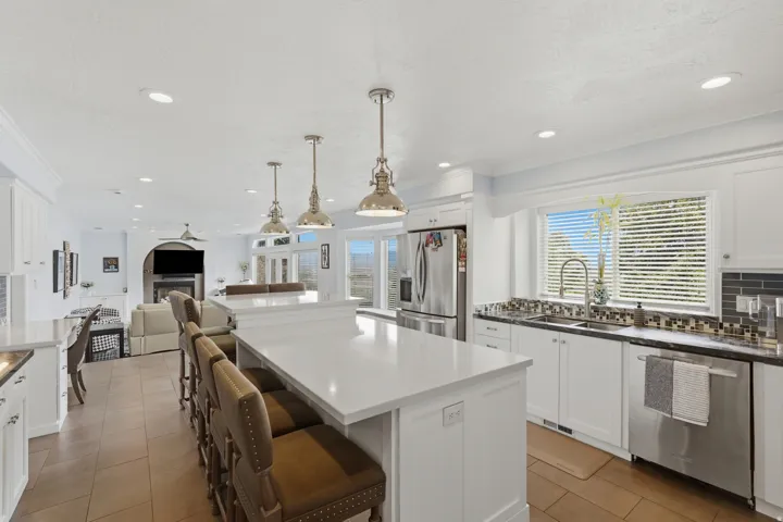 Expansive kitchen island with a light-toned countertop, stainless steel appliances, white cabinetry, and recessed lighting