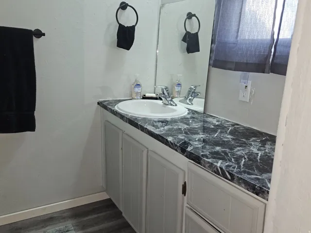 Dual sink vanity with a patterned countertop, white cabinetry, and wood-finish flooring