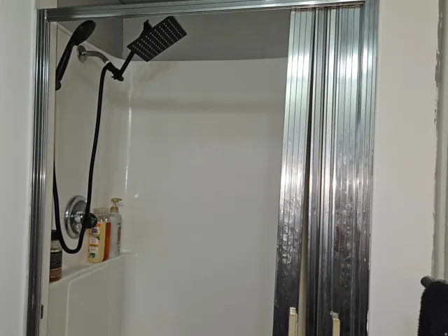 Shower stall with white surround, chrome shower fixtures, and a black handheld showerhead