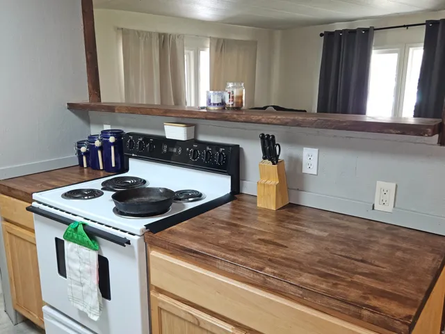 Kitchen featuring wood-finish countertops, natural wood-tone cabinetry, and a white electric range