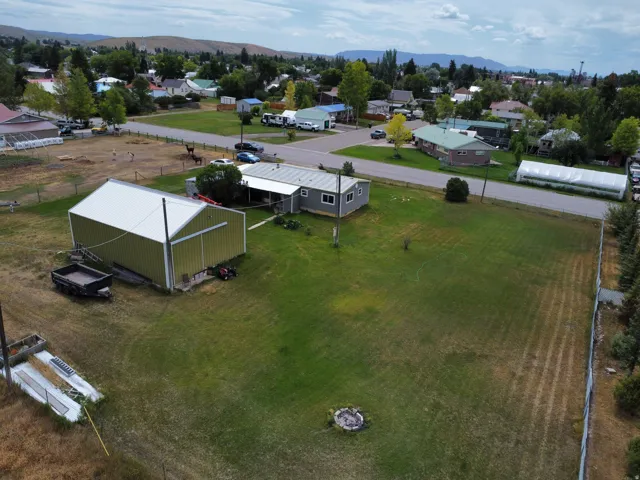 Expansive residential lot featuring mature landscaping, open green space, and multiple outbuildings including a metal-frame structure and mobile home
