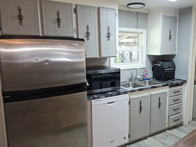 Light gray cabinetry with ornate black hardware, black and white speckled countertops, stainless steel refrigerator, and recessed lighting