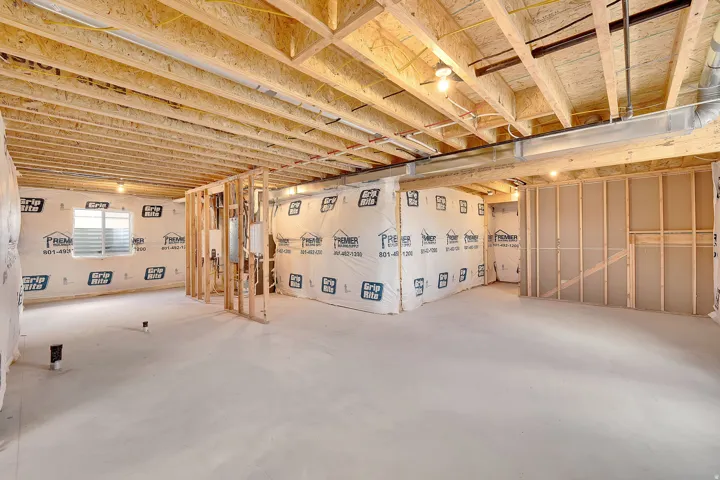 Unfinished basement featuring a concrete floor, framed walls, exposed ceiling joists, and a window with blinds