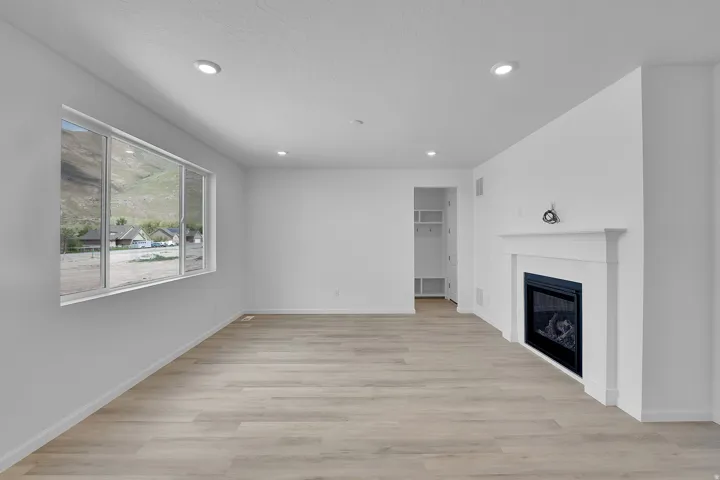 Open-concept living area with wood-finish flooring, recessed lighting, and a white mantle fireplace