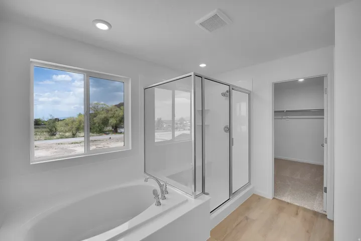 Soaking tub, walk-in shower with glass enclosure, recessed lighting, wood-finish flooring, and a window