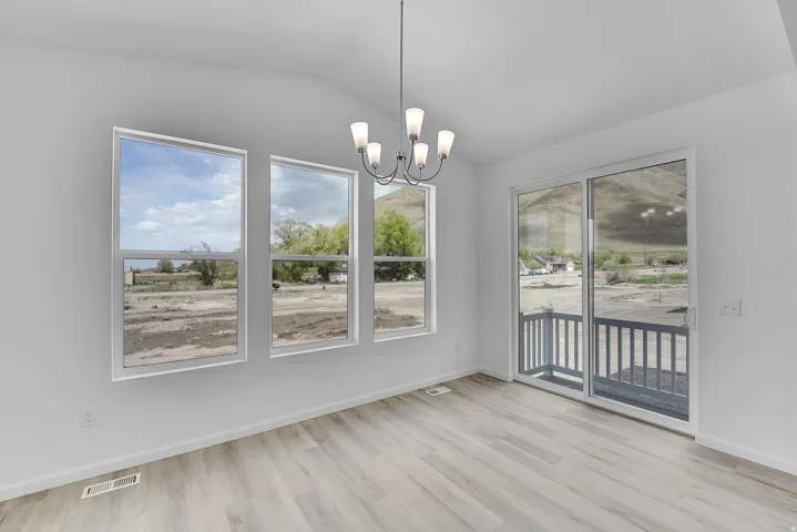 Vaulted ceiling, wood-finish flooring, contemporary chandelier, multiple windows, and a sliding glass door with a balcony