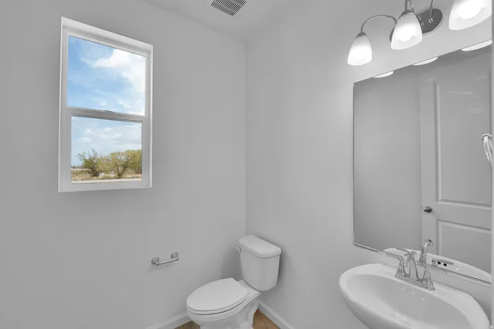 Pedestal sink with chrome faucet, wall-mounted mirror, three-light vanity fixture, and window