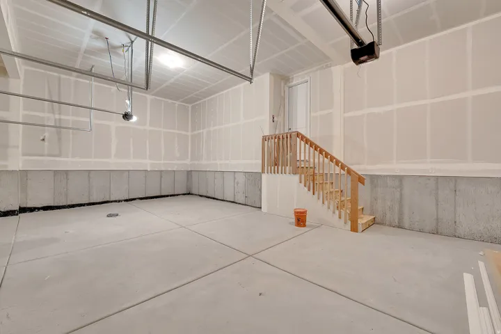 Concrete flooring with expansion joints, unfinished walls, wooden stairway with railing, and a white interior door