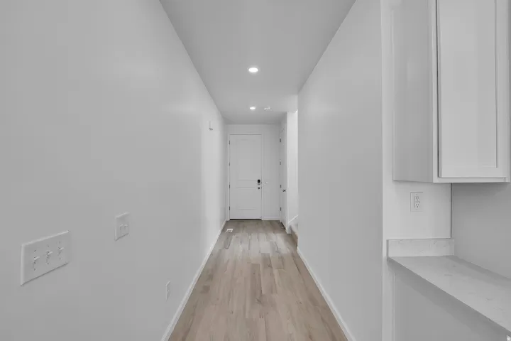 Hallway with wood-finish flooring, recessed lighting, and a solid core door
