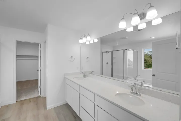 Dual vanity with undermount sinks, expansive countertop, large mirror, and wood-finish flooring