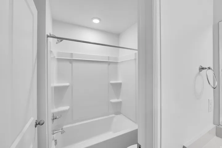 Bathtub with integrated shower, chrome fixtures, and recessed lighting