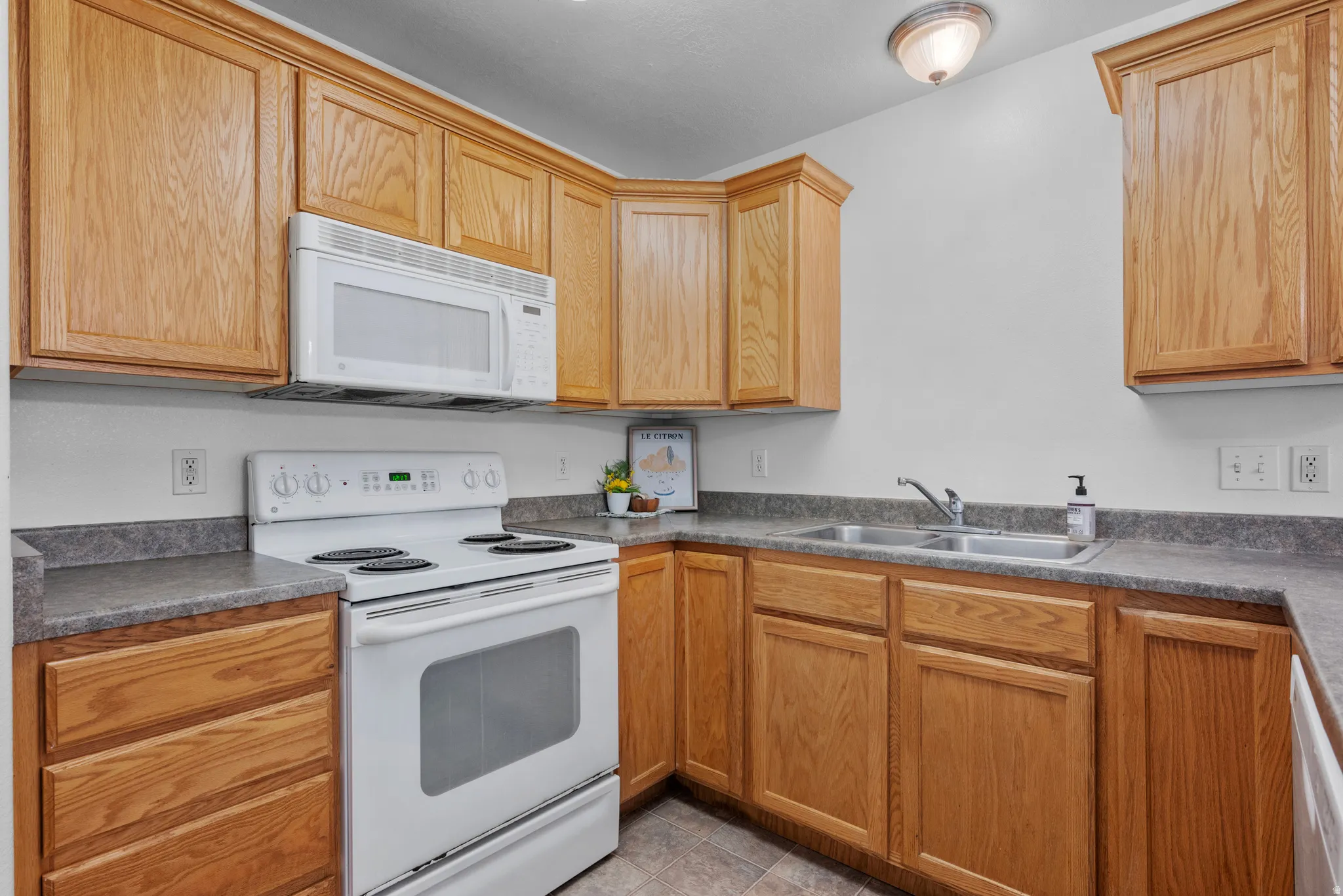 Wood-finish cabinetry with crown molding, laminate countertops, stainless steel double-basin sink, and a white electric range with an over-the-range microwave