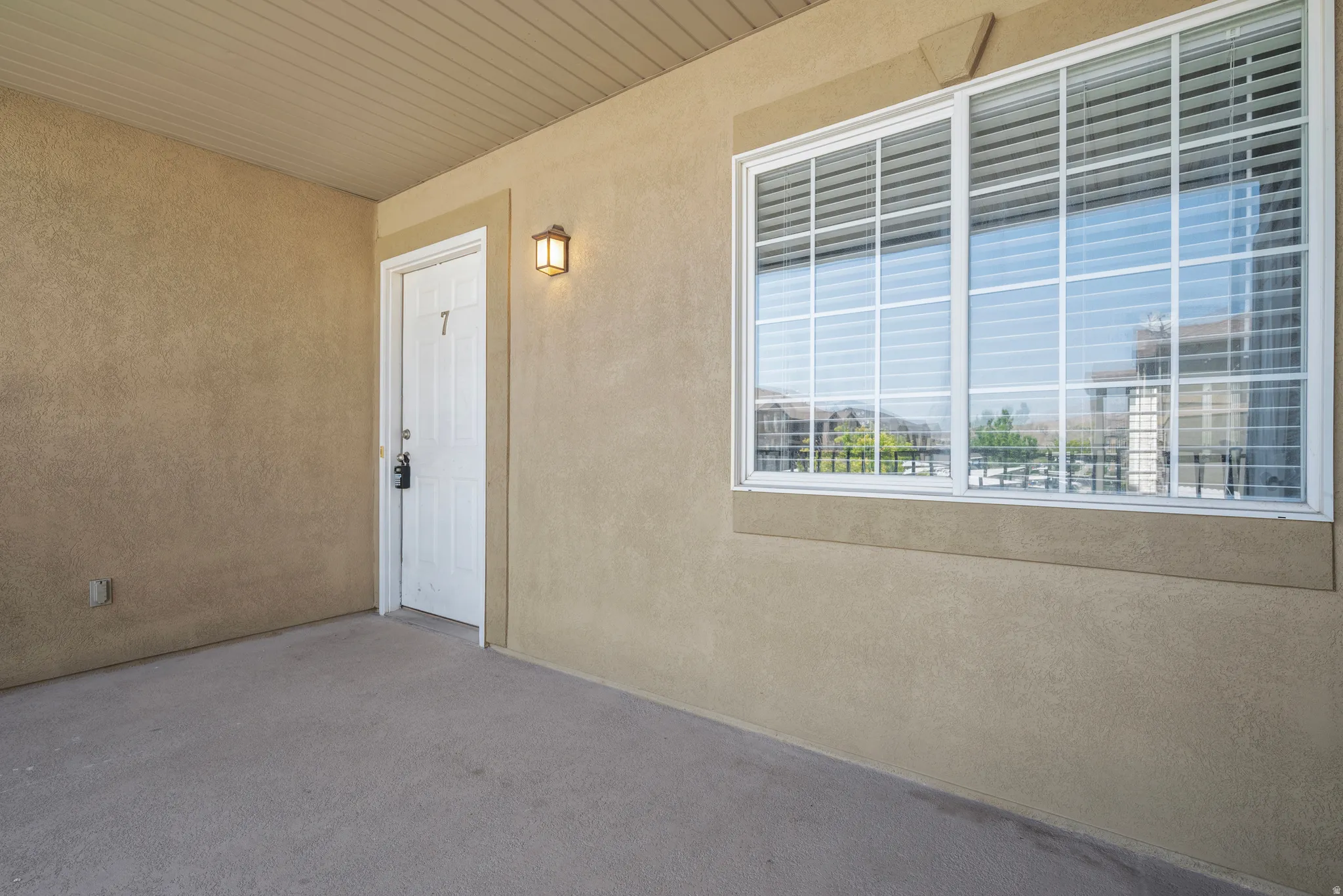 Covered entry with stucco exterior, a single entry door, and a large window with grilles and blinds