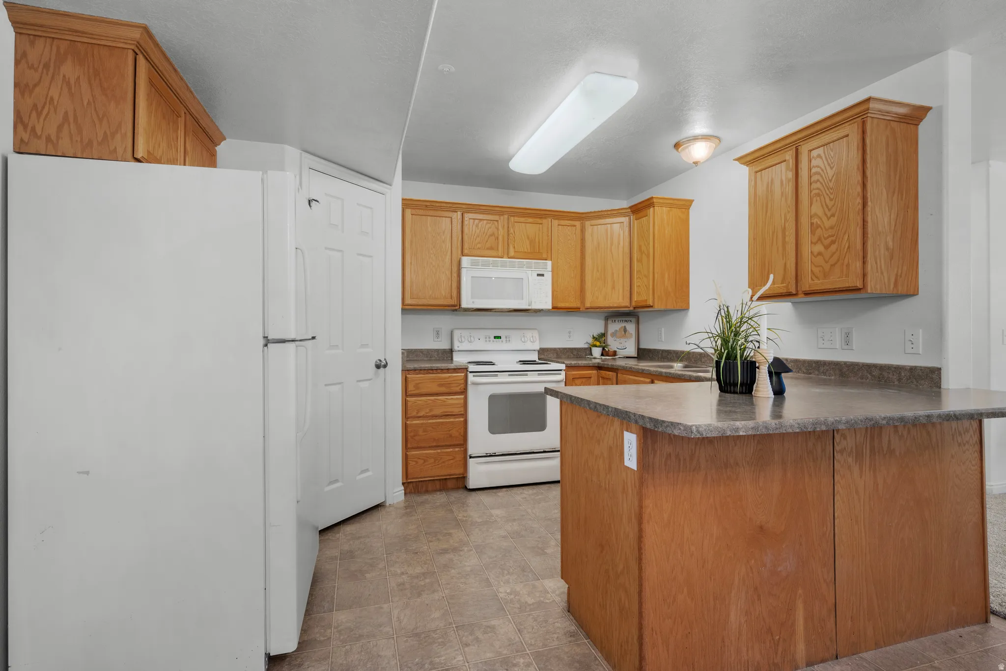 Kitchen featuring wood cabinetry, white appliances, durable countertops, and a central island with a breakfast bar