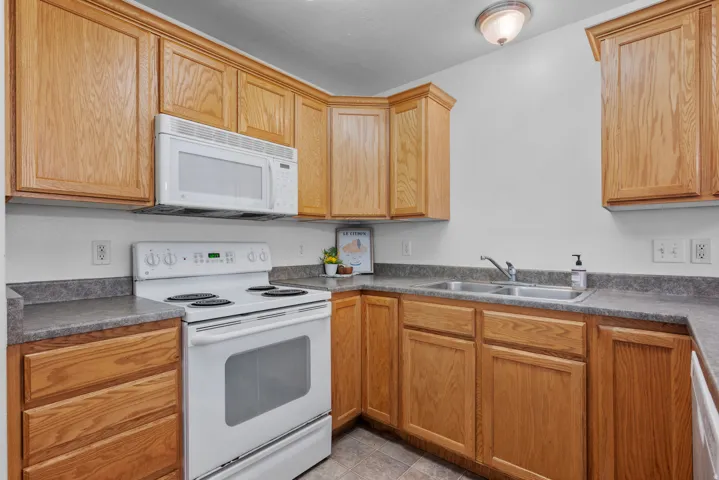 Wood-finish cabinetry with crown molding, laminate countertops, stainless steel double-basin sink, and a white electric range with an over-the-range microwave