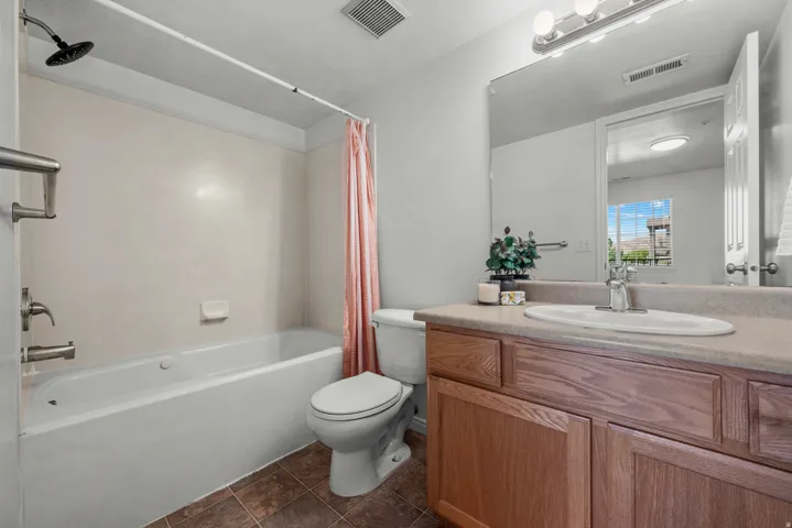 White bathtub and shower combination with a black shower head, wood-finish vanity with a single basin sink, and a large wall-mounted mirror