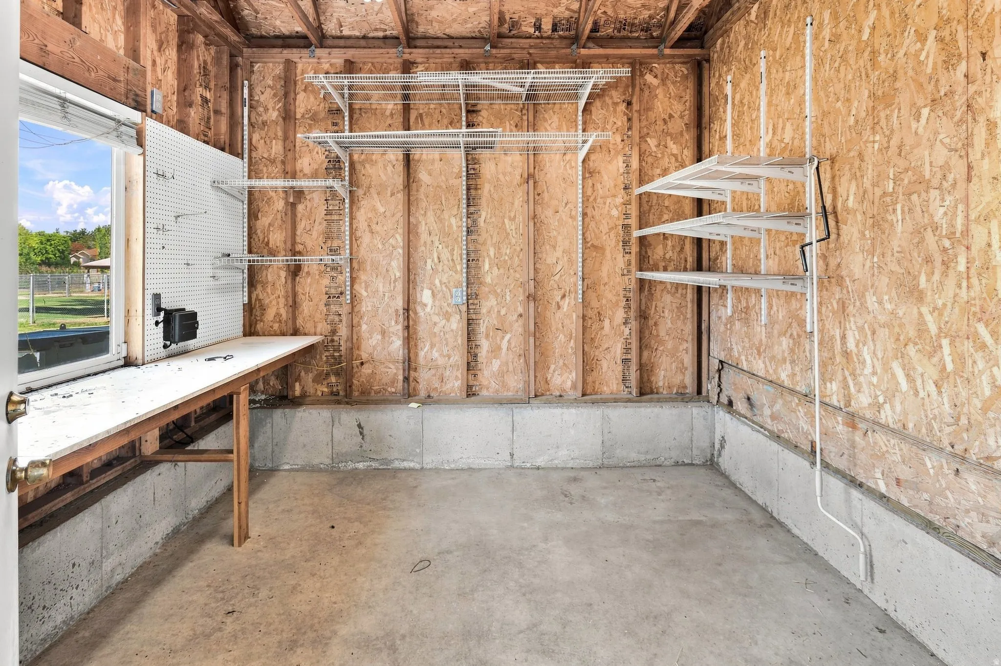 Concrete flooring with a built-in workbench, pegboard, and multiple wall-mounted shelving units