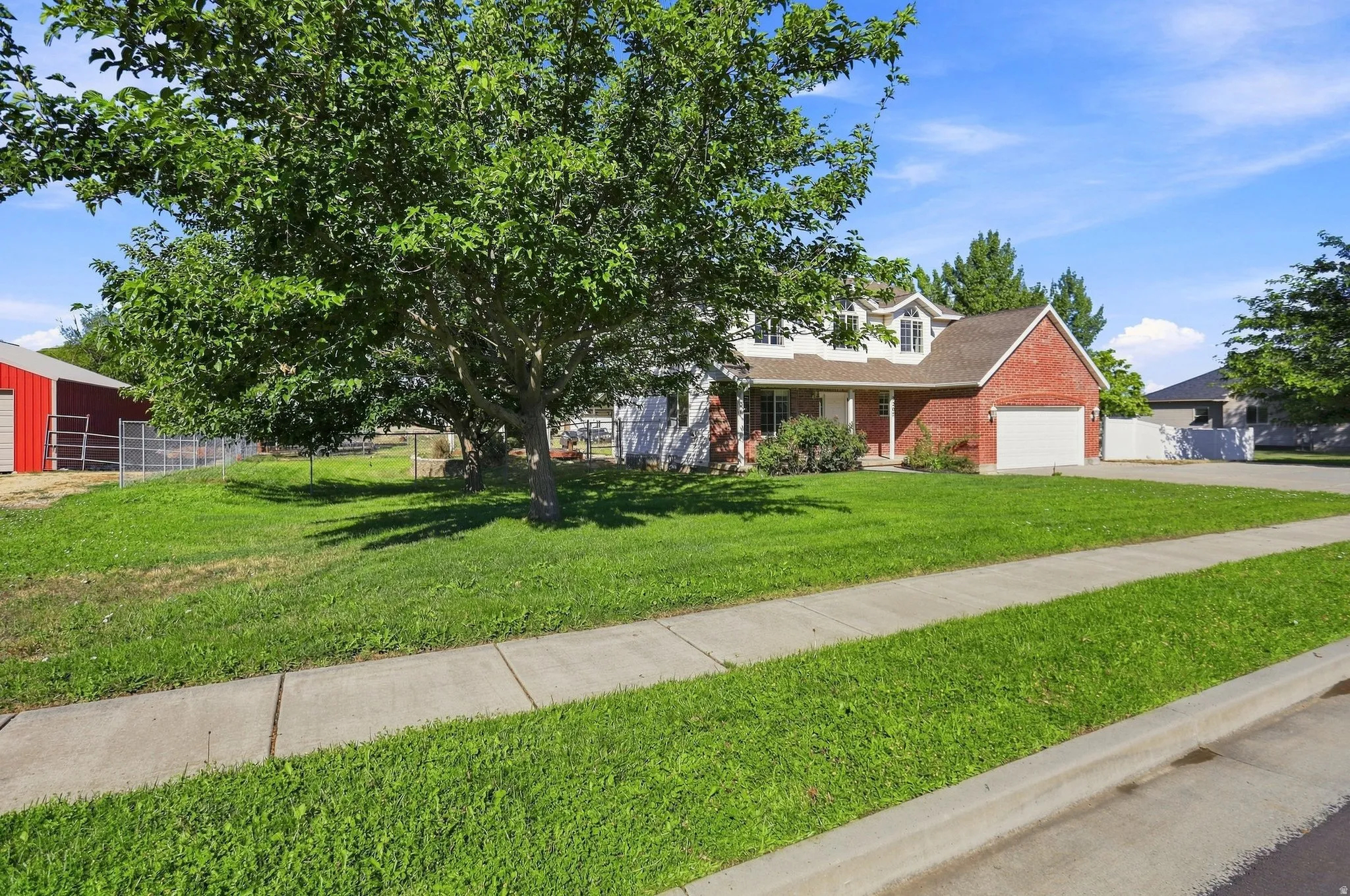 Spacious front yard with mature trees, a red brick facade, white trim, a white garage door, and a covered front porch