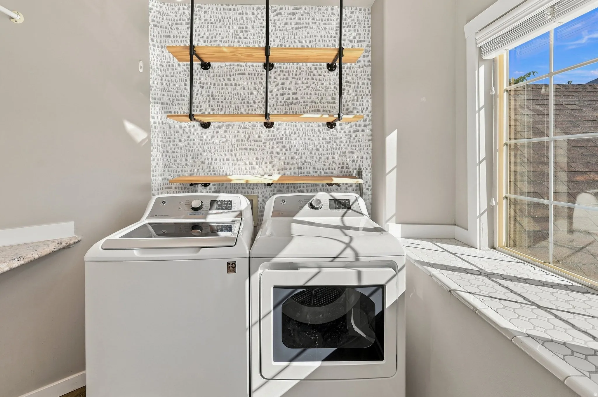 Utility space featuring a window with integrated blinds, hexagonal tiled windowsill, wall-mounted wood shelves, and a patterned accent wall