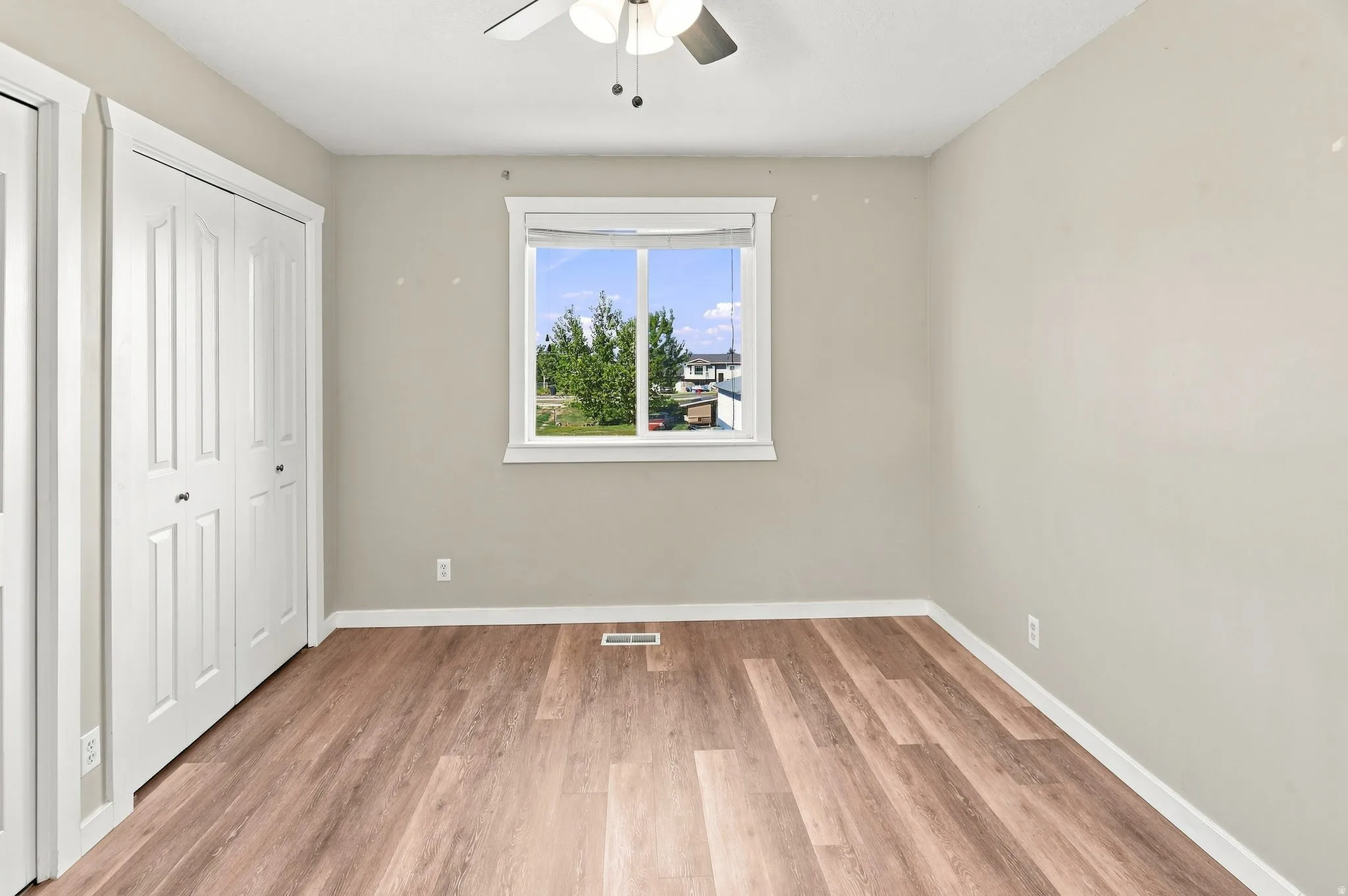 Wood-finish flooring with white trim, a double bi-fold closet, and a ceiling fan