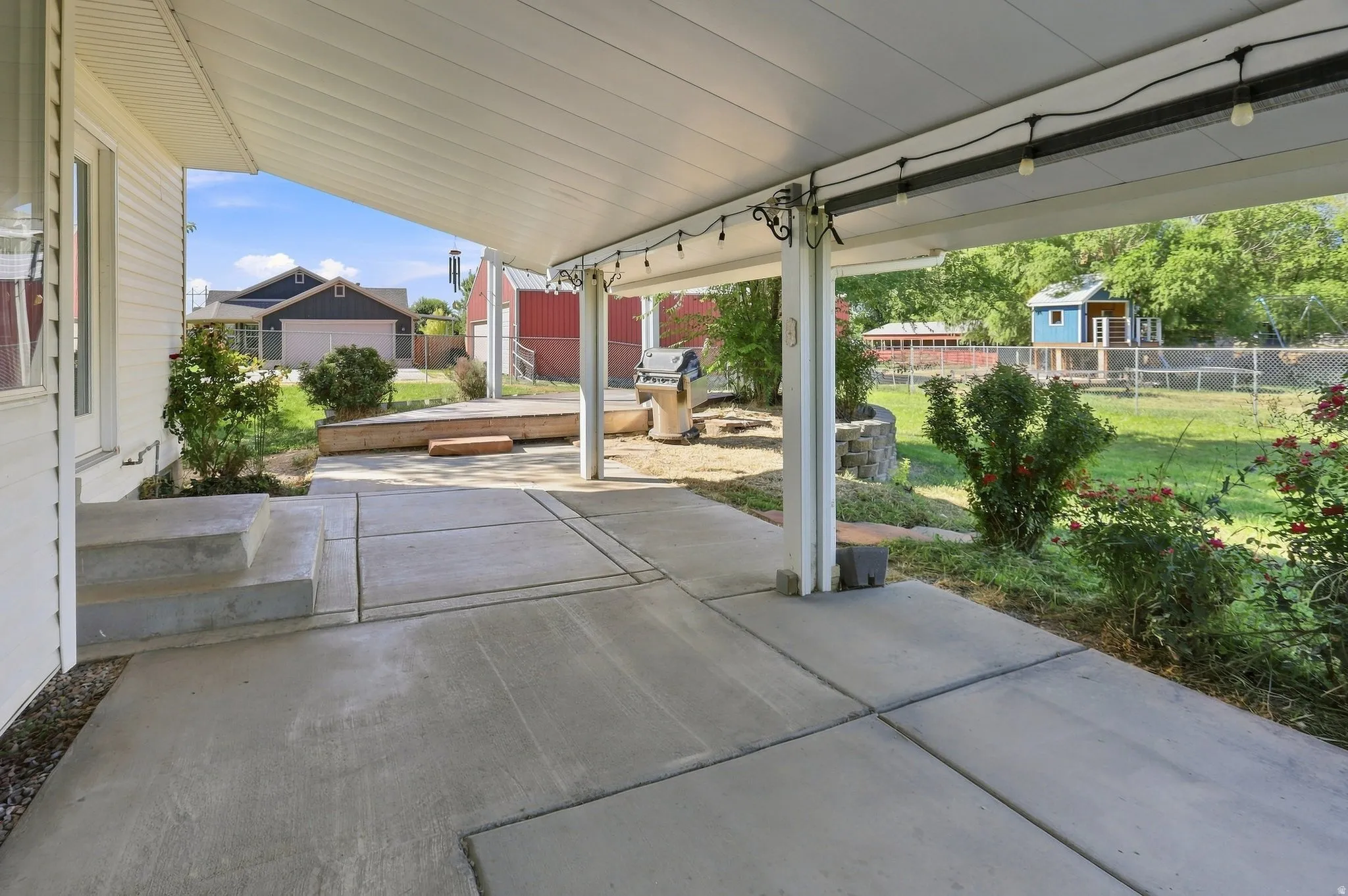 Covered patio with concrete flooring, supported by white columns, and featuring string lighting