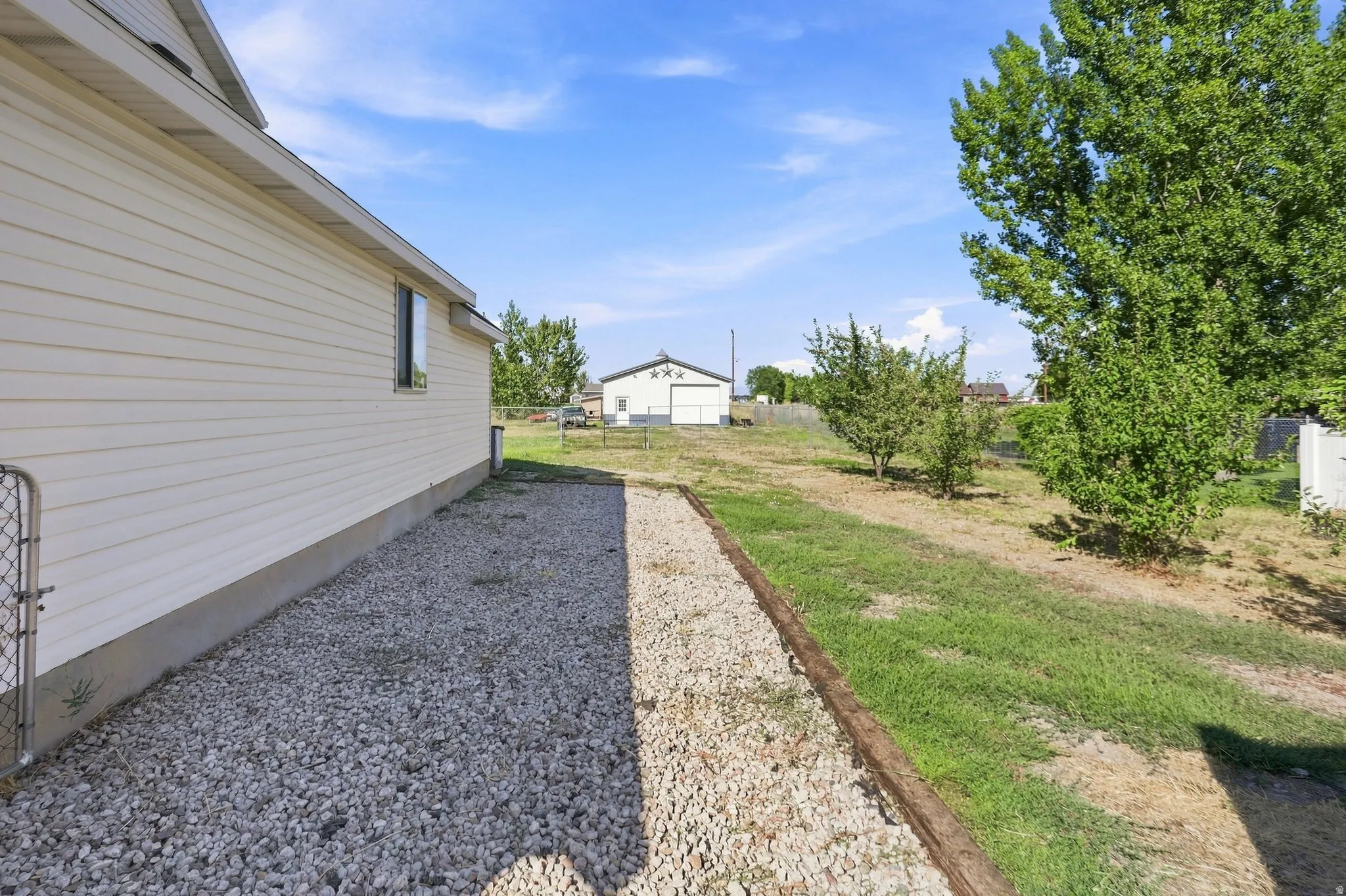 Property exterior featuring horizontal siding and a gravel perimeter, complemented by a grassy area with established trees
