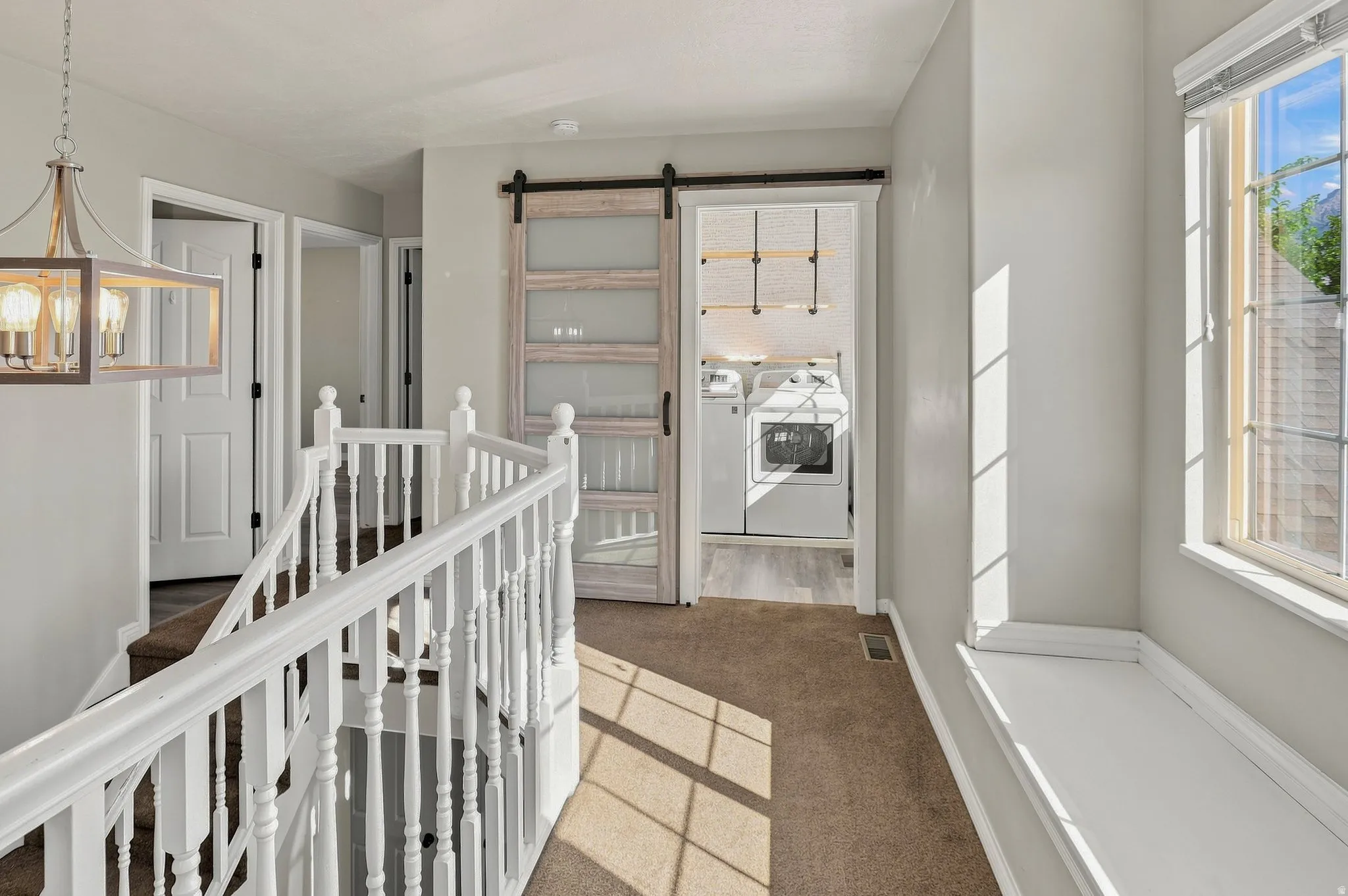 Staircase with white wood spindles, gray wall paint, wood-finish flooring, a window with a built-in sill, and a barn door with frosted glass panels