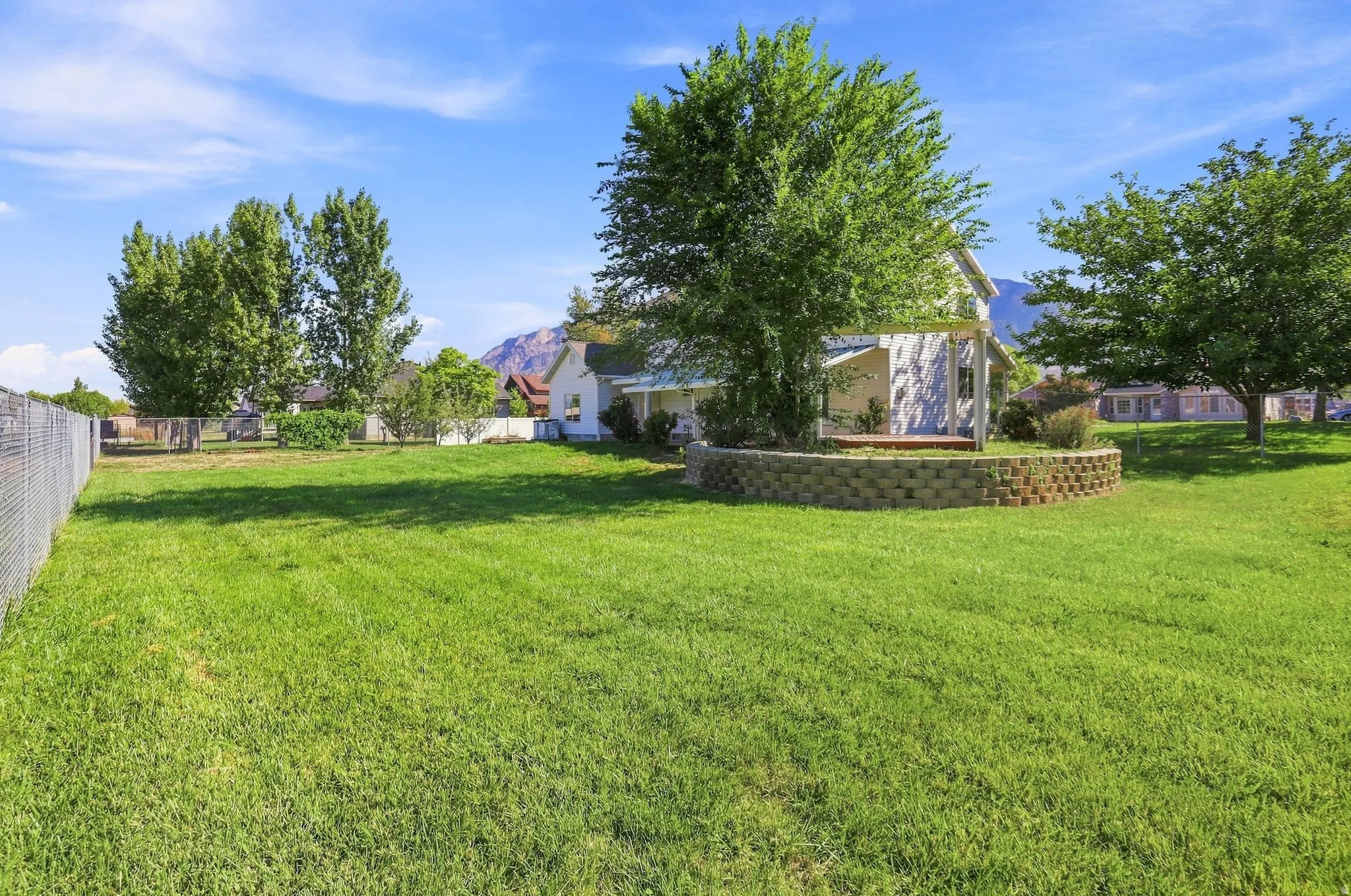 Expansive lawn area featuring mature trees and a decorative stone retaining wall