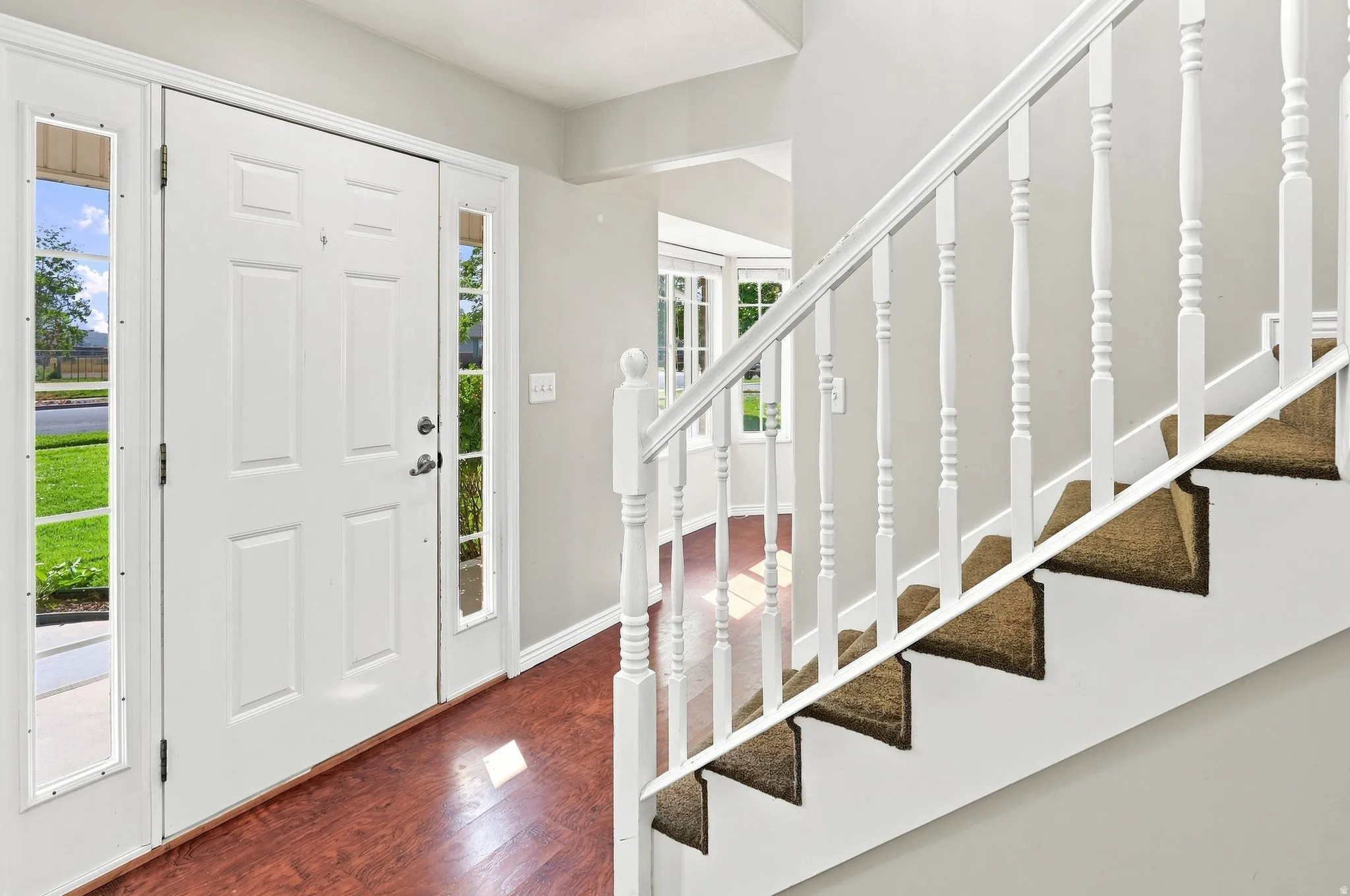 Entryway with wood-finish flooring, white paneled door with sidelight windows, and a staircase featuring white balusters and carpeted treads