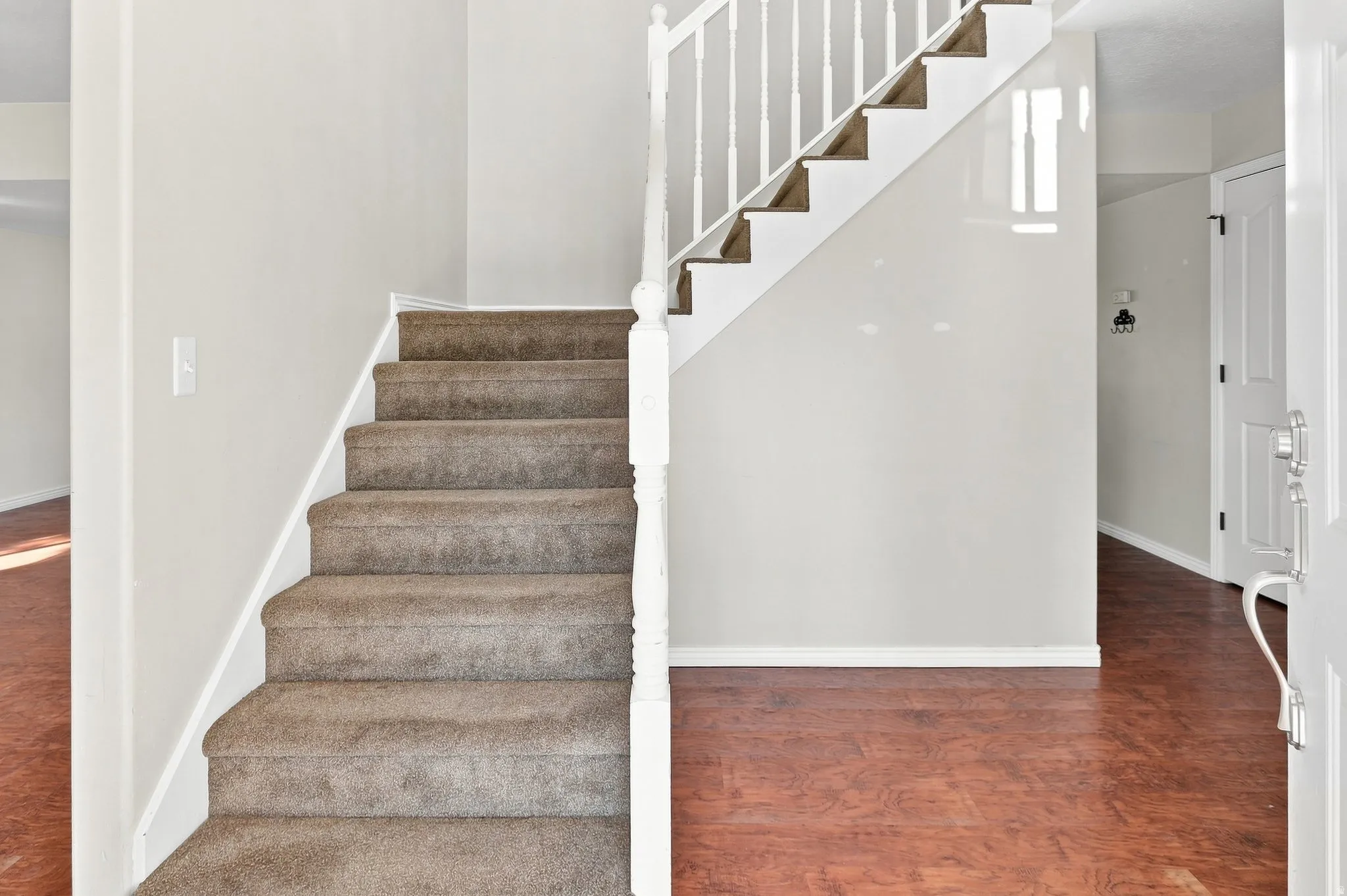 Staircase featuring carpeted treads and white wood balusters, complemented by wood-finish flooring