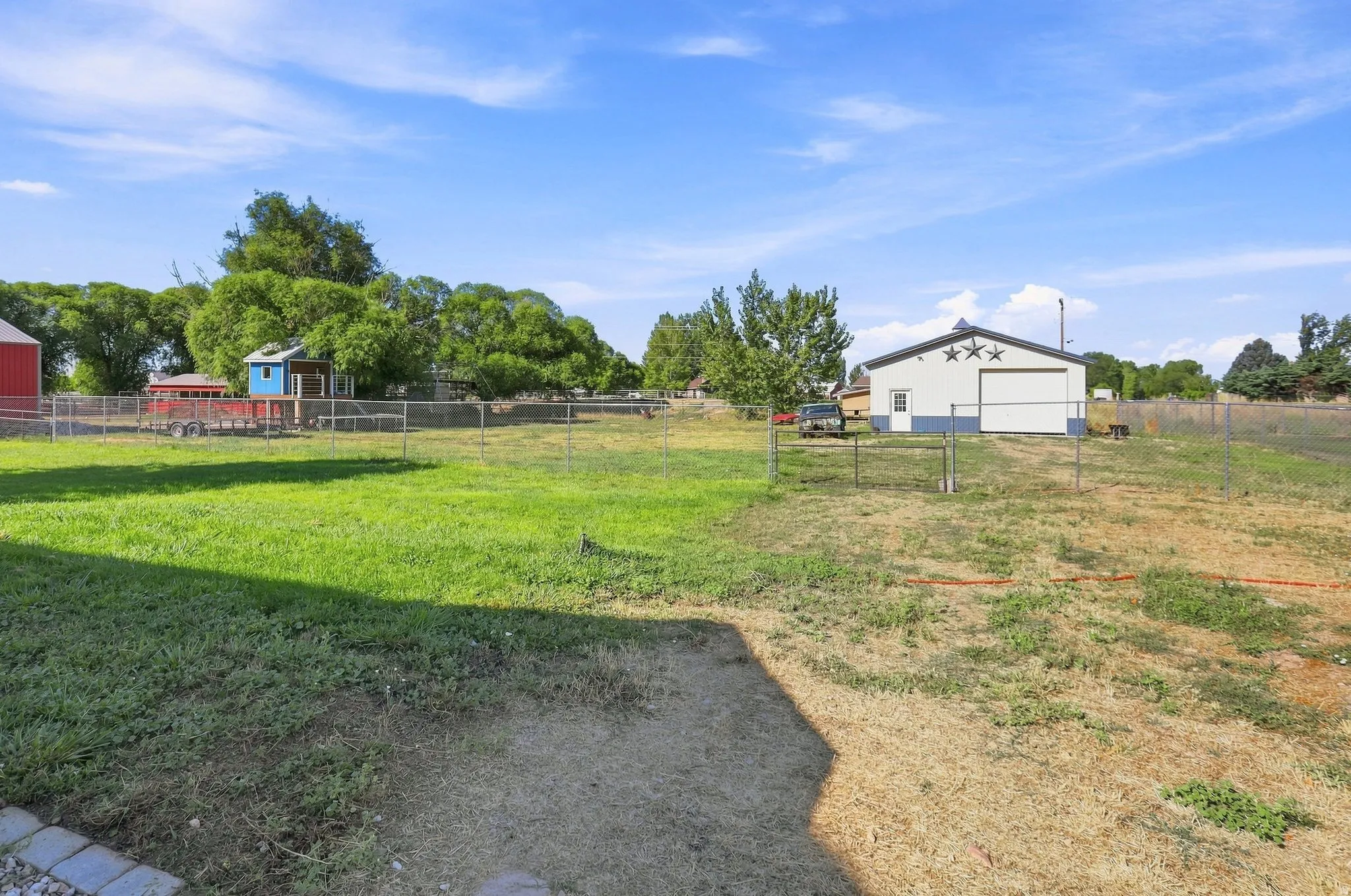 Expansive outdoor space featuring a large grassy area, a red barn structure, and a white outbuilding with a prominent garage door