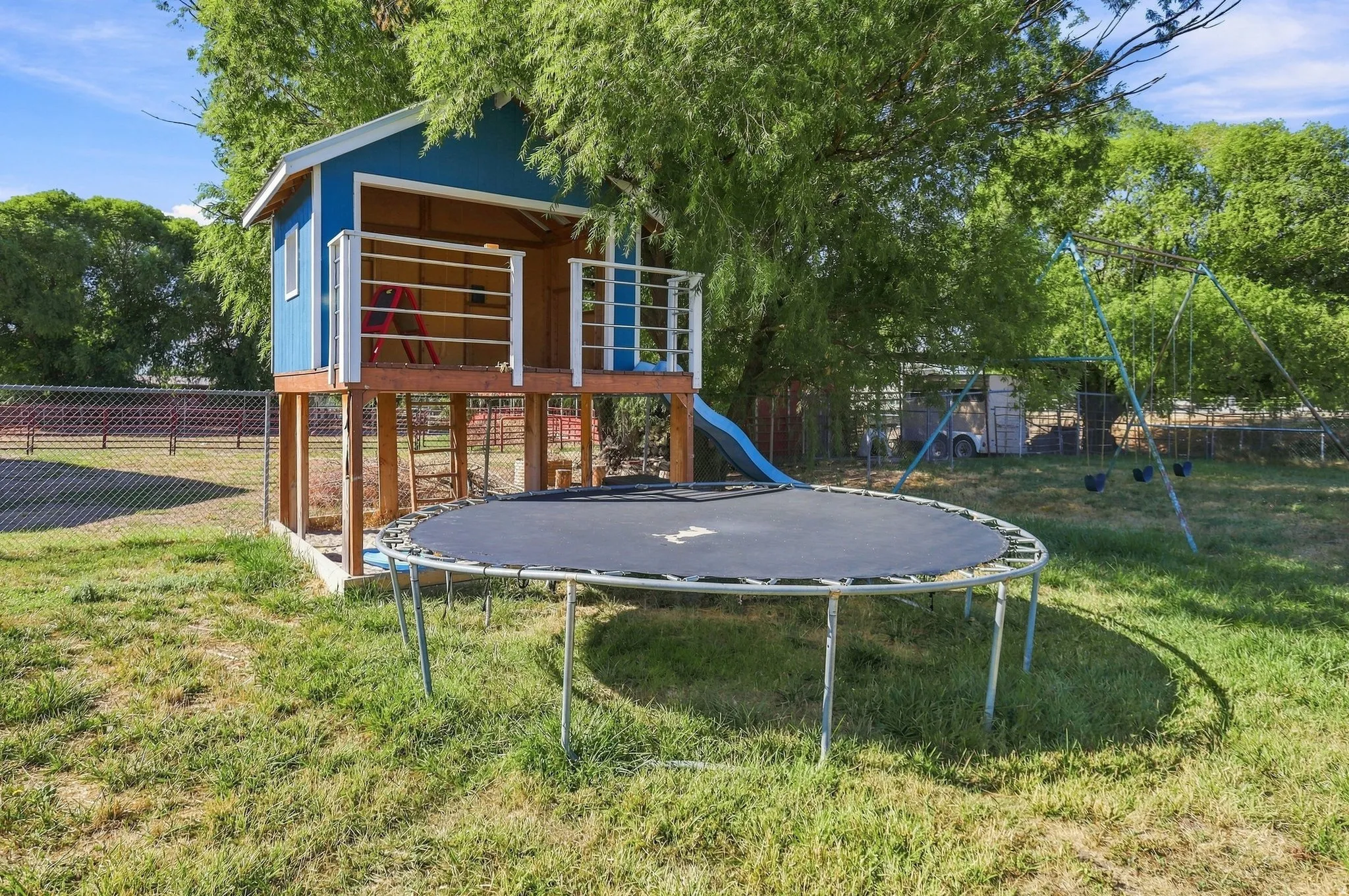 Play structure featuring an elevated platform with a slide, a swing set, and a mature tree