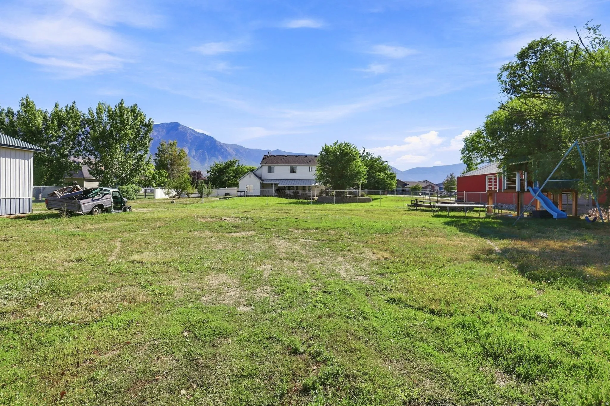Expansive grassy yard with mountain scenery, surrounded by mature trees, featuring a red shed