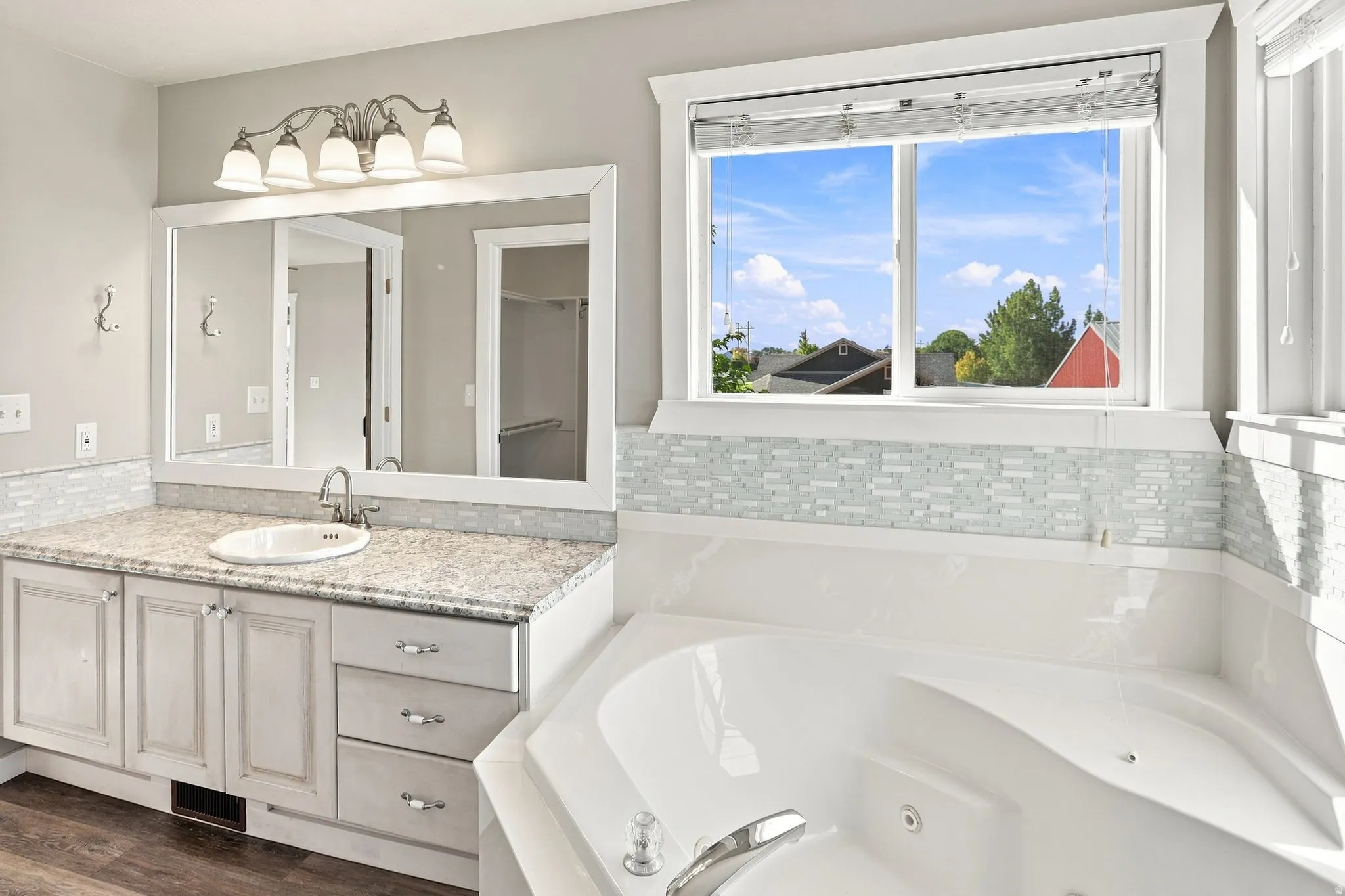 Deep soaking tub, dual-pane window, vanity with integrated sink, stone-finish countertop, and decorative tile backsplash