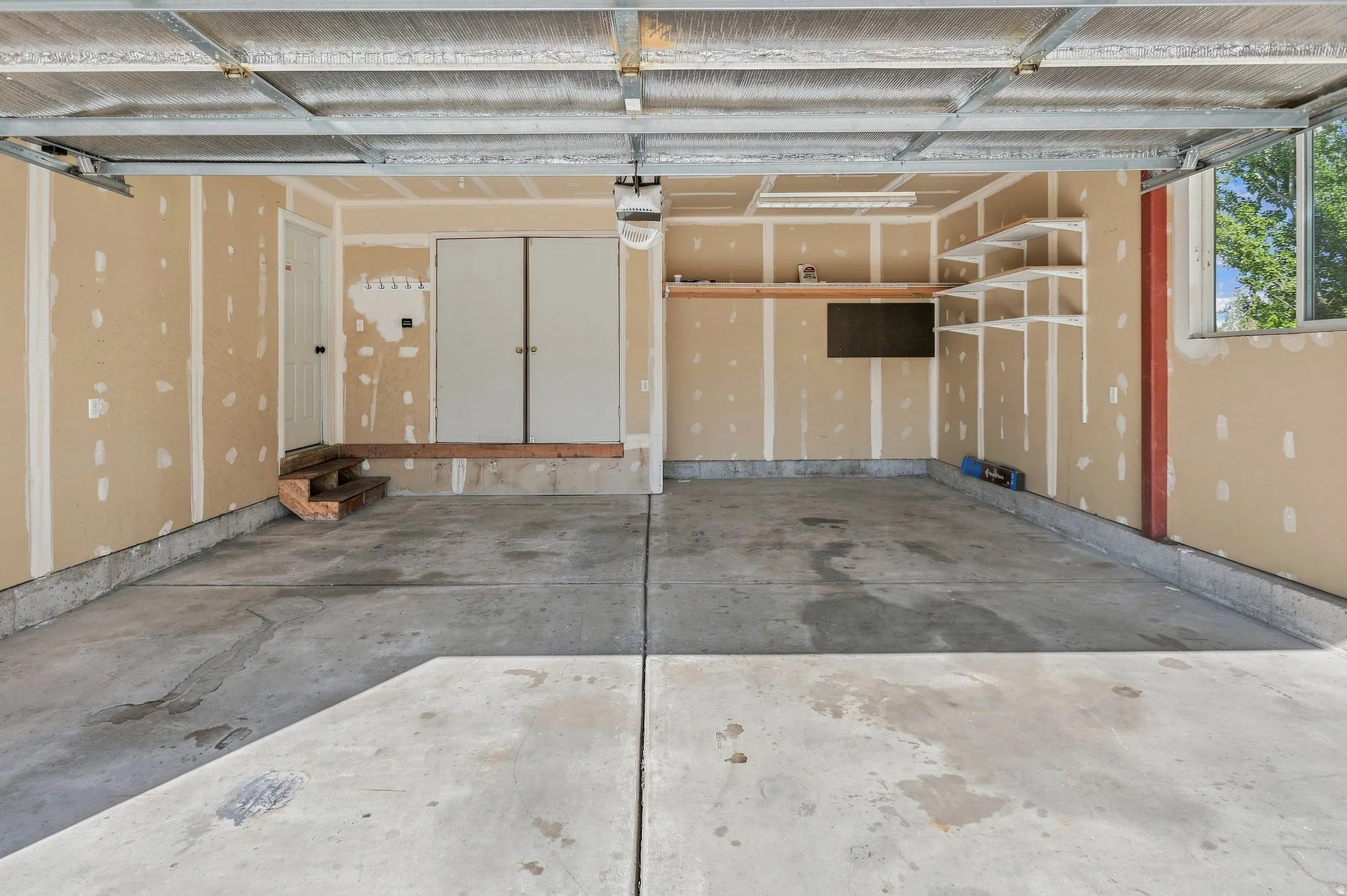 Spacious garage featuring concrete flooring, built-in shelving, an interior access door, and a window for natural light