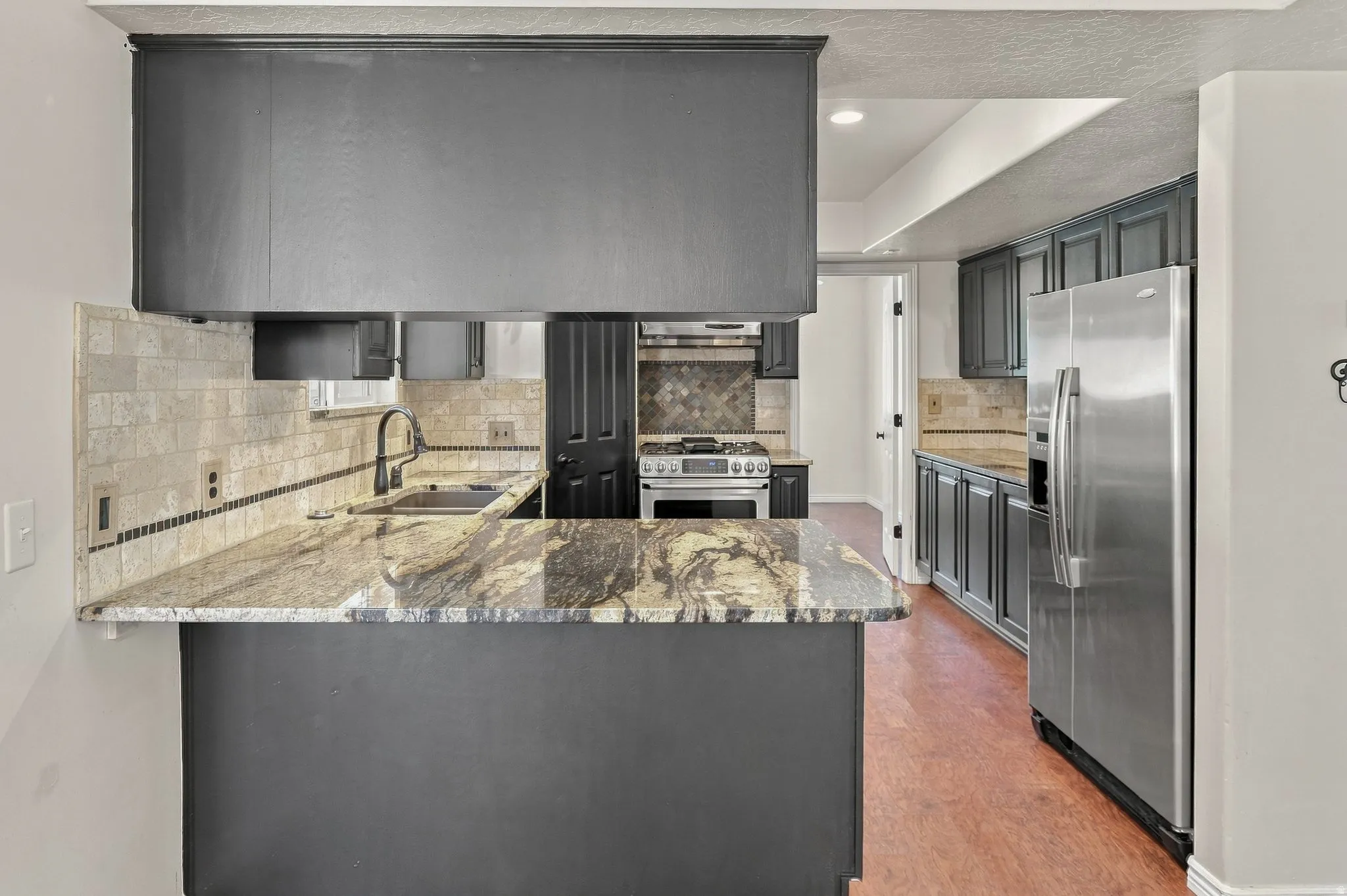 Kitchen featuring dark cabinetry, stainless steel appliances, speckled countertops, and a tiled backsplash