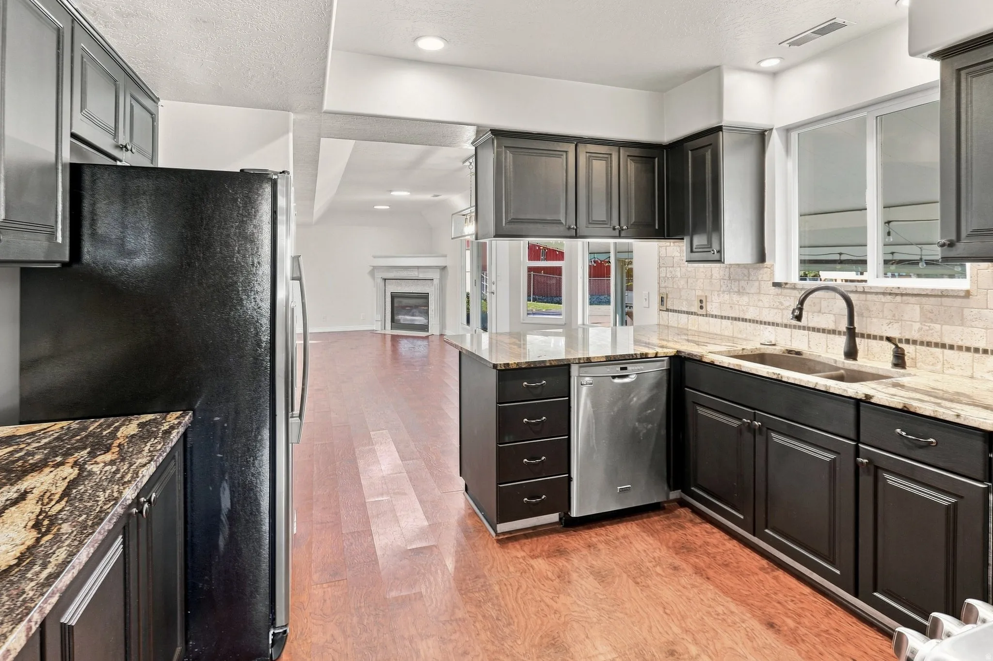 Kitchen featuring dark cabinetry, light-toned countertops, a stainless steel dishwasher, a black refrigerator, and wood-finish flooring