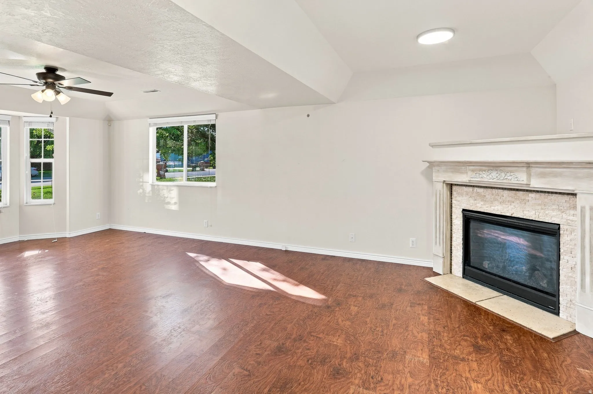 Spacious room featuring wood-finish flooring, multiple windows, and a built-in fireplace with a decorative mantel and stone surround