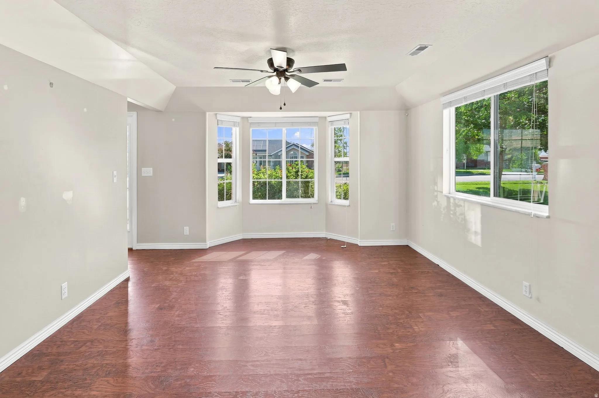 Spacious room featuring wood-finish flooring, light-toned walls, and multiple windows