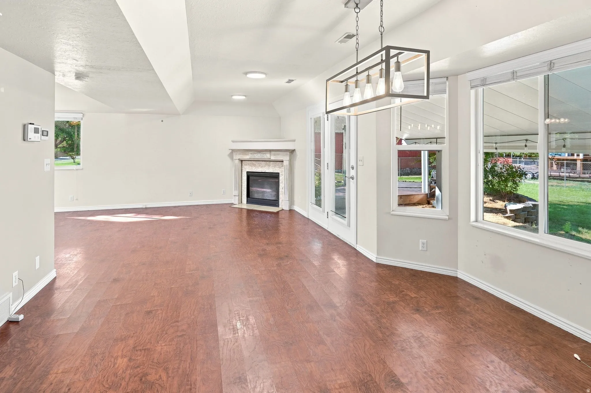 Wood-finish flooring throughout, featuring a corner fireplace with a stone surround, recessed lighting, and a modern rectangular chandelier
