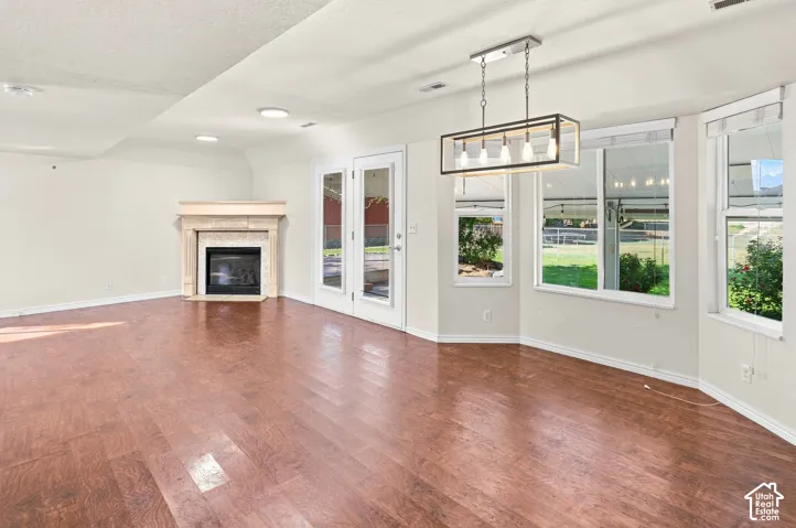 Wood-finish flooring, a fireplace with a stone surround, double French doors, a linear chandelier, and multiple windows