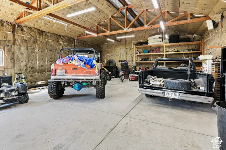 Spacious garage with exposed wood trusses, ample overhead lighting, concrete flooring, and built-in shelving