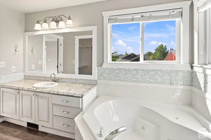 Deep soaking tub, dual-pane window, vanity with integrated sink, stone-finish countertop, and decorative tile backsplash
