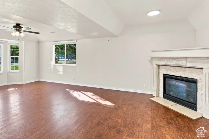 Spacious room featuring wood-finish flooring, multiple windows, and a built-in fireplace with a decorative mantel and stone surround